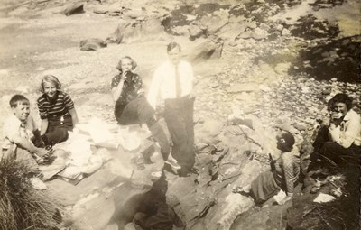 Four women, a man, and two children having a beach picnic