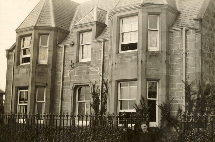 Woman standing at the entrance gate to a house ~ Clashmore ?