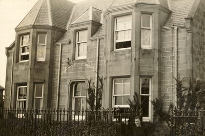 Woman standing at the entrance gate to a house ~ Clashmore ?