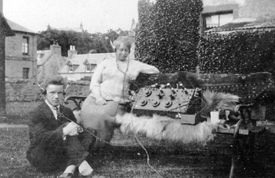Man and woman, with headphones connected to an early radio set