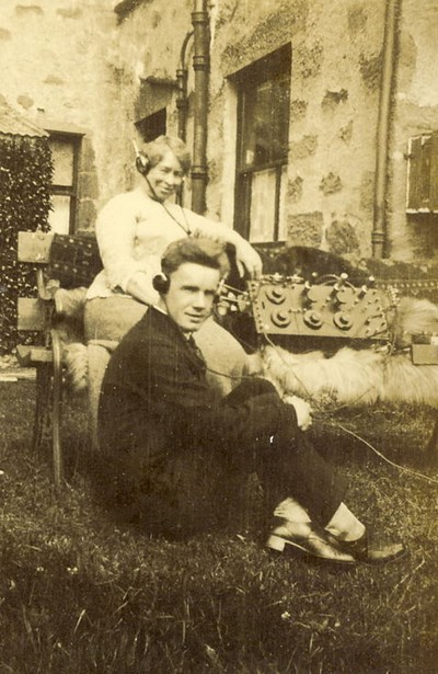 Man and woman, with headphones connected to an early radio set
