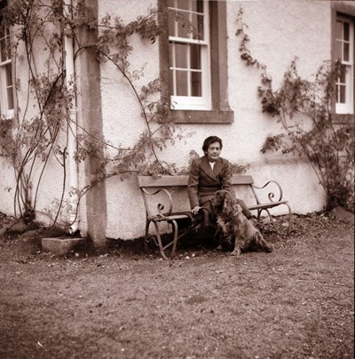 Lady sitting outside a house, with a dog.